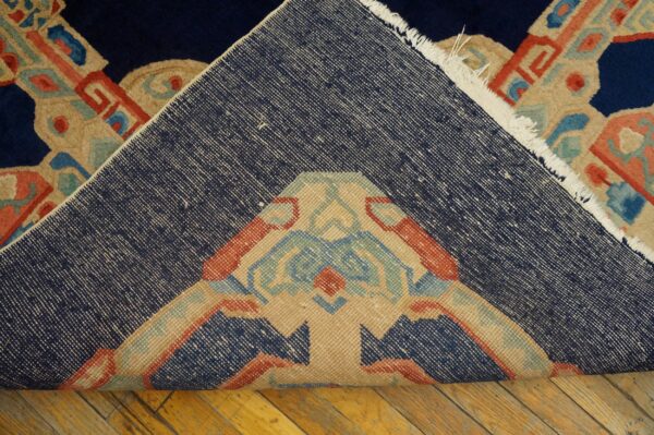 The rug is folded to show its tightly woven navy backing above the colorful low-pile geometric pattern on wood.