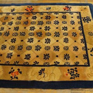 Gold and tan rug with a navy floral lattice pattern and thick navy border on wood flooring.