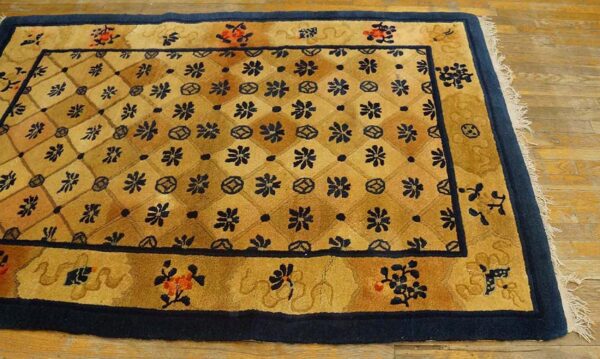 Gold and tan rug with a navy floral lattice pattern and thick navy border on wood flooring.
