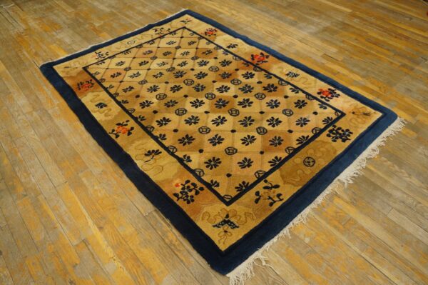 Gold rug with a navy and red lattice pattern border rests on worn wooden floorboards.