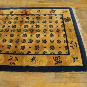 A golden yellow rug with a navy floral grid pattern and wide border sits on distressed wooden planks.