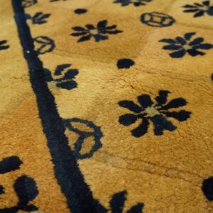 Close-up of a gold rug featuring scattered navy blue stylized floral and geometric patterns with a visible medium pile.