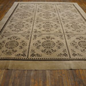 Beige rug with a dark brown grid and medallion pattern is displayed on worn wood floorboards.