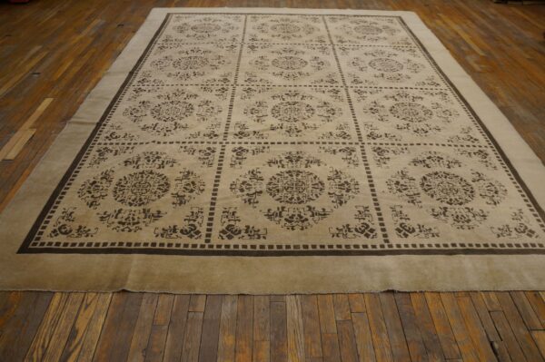 Beige rug with a dark brown grid and medallion pattern is displayed on worn wood floorboards.