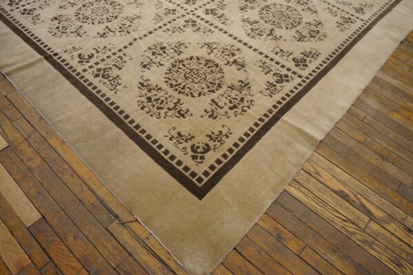 Corner view of a low-pile beige rug with dark brown diamond patterns on worn wooden plank flooring.