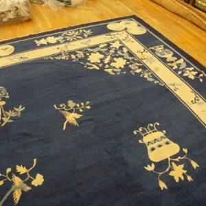 Navy blue rug with a wide cream border featuring stylized flowers and bird motifs on wood flooring.