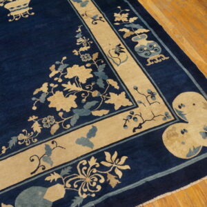 Close-up of a navy rug with tan and blue ornate floral borders displayed on wood planks.