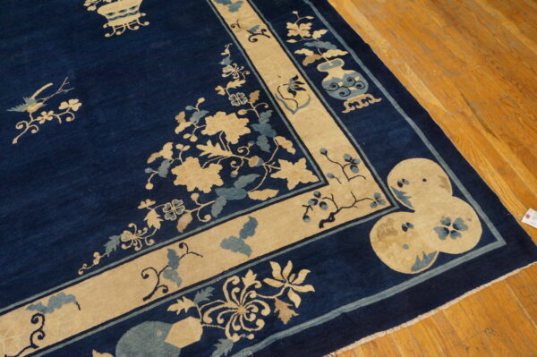 Close-up of a navy rug with tan and blue ornate floral borders displayed on wood planks.