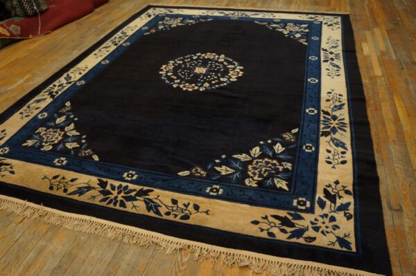 Deep navy rug with cream and blue floral borders features a central medallion on plank hardwood floors.