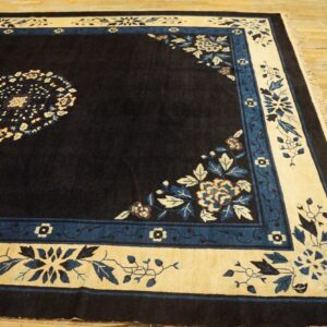 Navy blue area rug with cream and blue floral borders and fringe rests on wood planks.