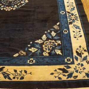 Close-up of a navy rug corner showing tan and blue floral borders on light wood flooring.