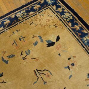 Tan rug with scattered blue and pink patterns, contrasted by a bold navy floral border on wood floors.