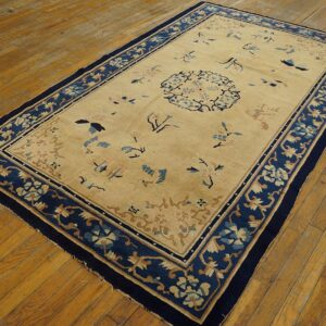 Low-pile beige rug featuring a navy blue border and scattered floral patterns on distressed wood flooring.