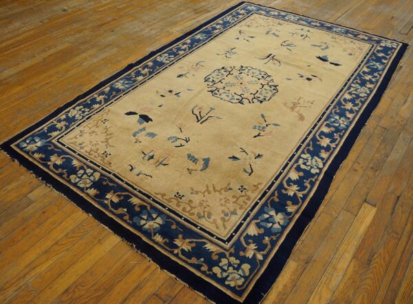 Antique peking chinese floral beige 1890s rug 2 Low-pile beige rug featuring a navy blue border and scattered floral patterns on distressed wood flooring.
