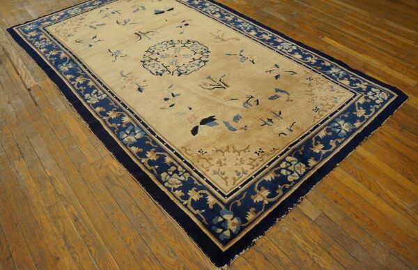 Antique peking chinese floral beige 1890s rug 3 Beige rug featuring scattered blue and tan floral designs and a wide navy border on distressed wood planks.