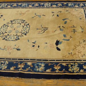 Traditional beige and navy blue rug with pink and light blue floral patterns on a wood floor.
