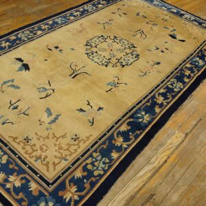 Rectangular gold rug with a navy border, scattered flowers, and a central medallion on wood planks.