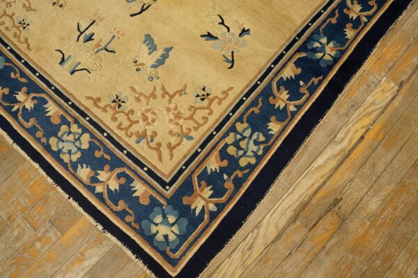 Antique peking chinese floral beige 1890s rug 7 Close-up of a tan rug with blue floral patterns and a wide navy border on light wooden floorboards.
