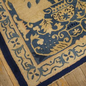 Detailed view of a low-pile rug featuring beige and blue scrollwork borders on distressed wood flooring.