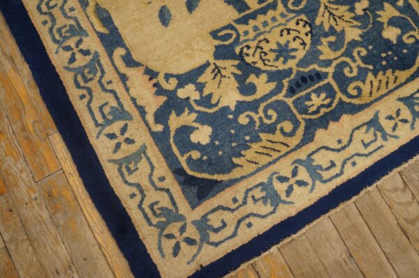 Detailed view of a low-pile rug featuring beige and blue scrollwork borders on distressed wood flooring.
