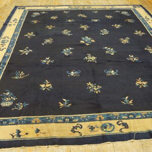 Navy area rug featuring blue and gold floral motifs bordered by wide tan and teal panels on wood flooring.