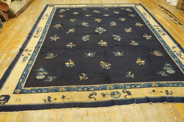 Large navy rug with scattered gold and teal designs and a wide beige border, lying on light wood floors.