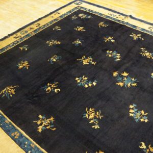 Navy rug featuring gold and teal floral sprays, bordered by wide tan panels, resting on wood flooring.