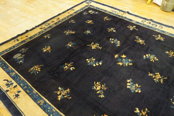 Navy rug featuring gold and teal floral sprays, bordered by wide tan panels, resting on wood flooring.