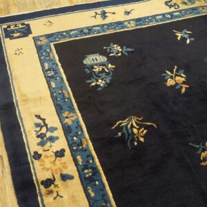 A dark navy rug with cream and teal borders and gold floral patterns rests on distressed wood flooring.