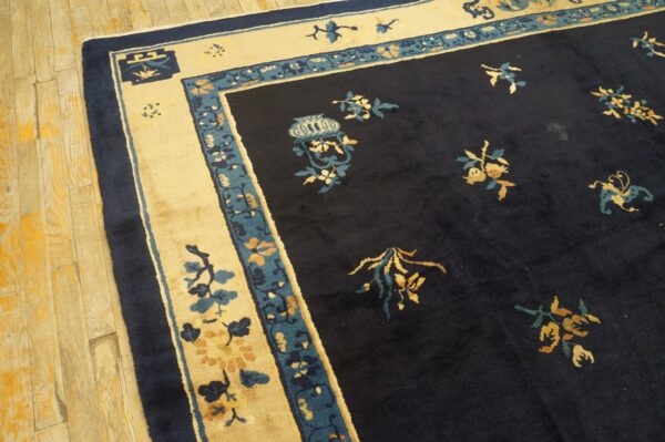 A dark navy rug with cream and teal borders and gold floral patterns rests on distressed wood flooring.