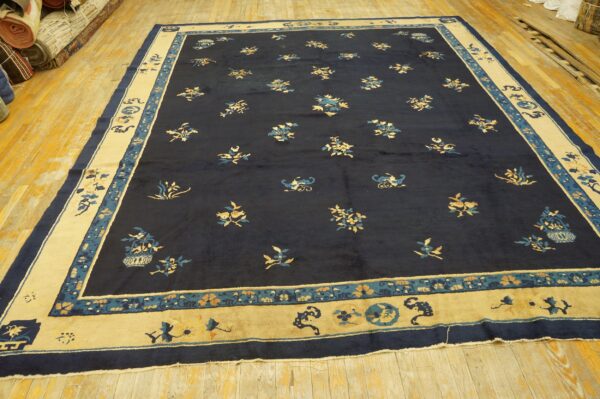 Low-pile navy rug with scattered gold and blue motifs and a thick cream border on hardwood.