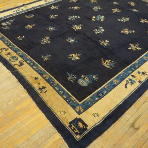 Navy blue rug with scattered floral patterns and wide mustard borders rests on worn plank wood flooring.