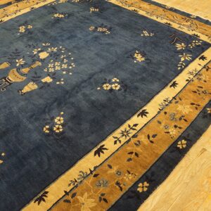 Dark blue rug with scattered gold floral motifs and vases features layered gold borders on hardwood flooring.