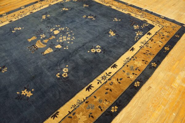 Dark blue rug with scattered gold floral motifs and vases features layered gold borders on hardwood flooring.