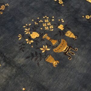 The deep blue rug field has yellow flowers and stylized urns, with a tan border visible above.