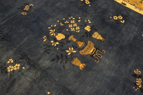 The deep blue rug field has yellow flowers and stylized urns, with a tan border visible above.