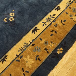 Navy blue rug with golden tan and brown floral borders resting on wooden plank flooring.