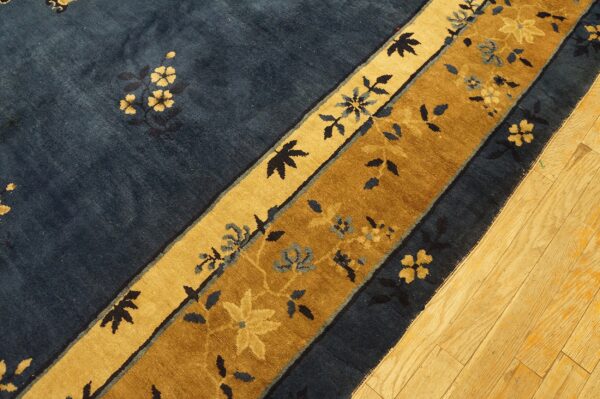Navy blue rug with golden tan and brown floral borders resting on wooden plank flooring.