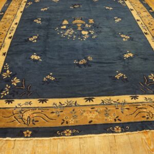 Blue rug with dense pile and scattered floral motifs features tan, gold, and blue ornate borders on wood flooring.