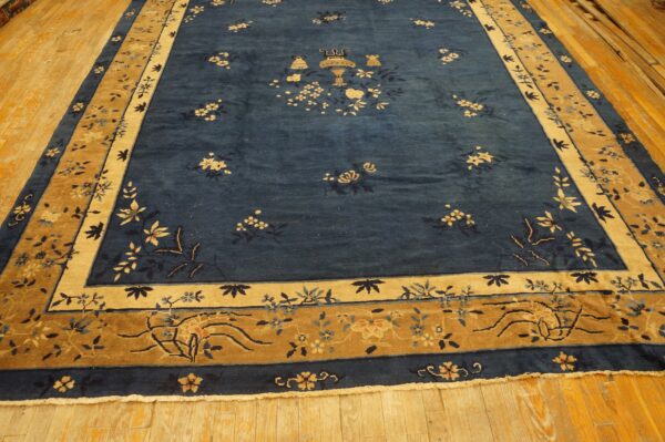 Blue rug with dense pile and scattered floral motifs features tan, gold, and blue ornate borders on wood flooring.