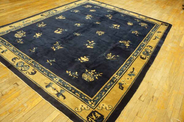A navy blue rug with scattered gold and teal floral patterns and a wide golden yellow border rests on wood planks.