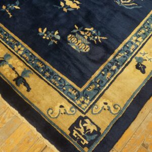 Corner detail of a navy blue rug with gold and teal floral borders on worn wood flooring.