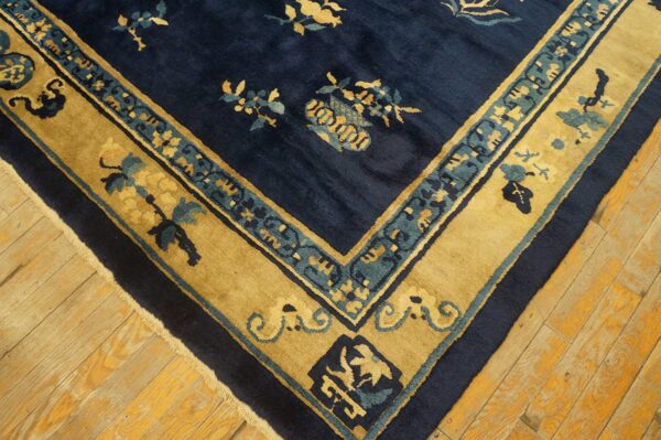 Corner detail of a navy blue rug with gold and teal floral borders on worn wood flooring.