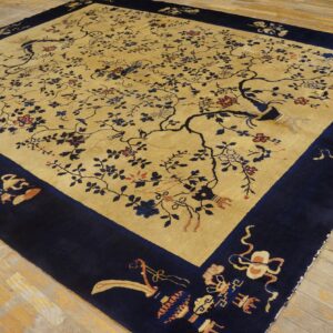 Large gold and navy rug with a detailed central field of branches, birds, and flowers on aged wooden floors.