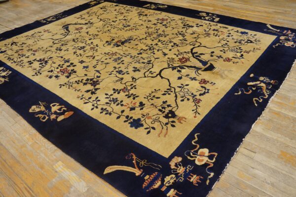 Large gold and navy rug with a detailed central field of branches, birds, and flowers on aged wooden floors.