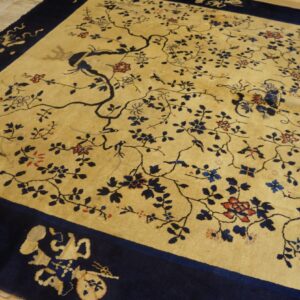 Tan rug with dark blue branches, birds, and red florals, framed by a wide navy border on wood flooring.