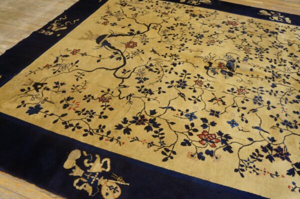 Tan rug with dark blue branches, birds, and red florals, framed by a wide navy border on wood flooring.