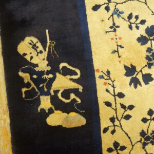 Navy blue and gold rug with a patterned figure and floral vines lying on distressed wood planks.