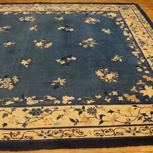 Dark blue field rug with contrasting cream and gold floral vine borders rests on light wood floors.