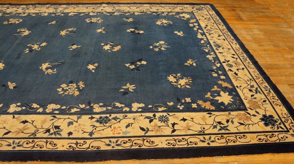 Dark blue field rug with contrasting cream and gold floral vine borders rests on light wood floors.